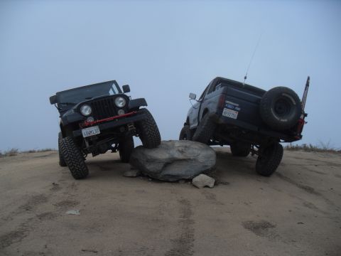 1990 Ford Bronco - Two off-road vehicles navigate a rocky landscape under an overcast sky.
