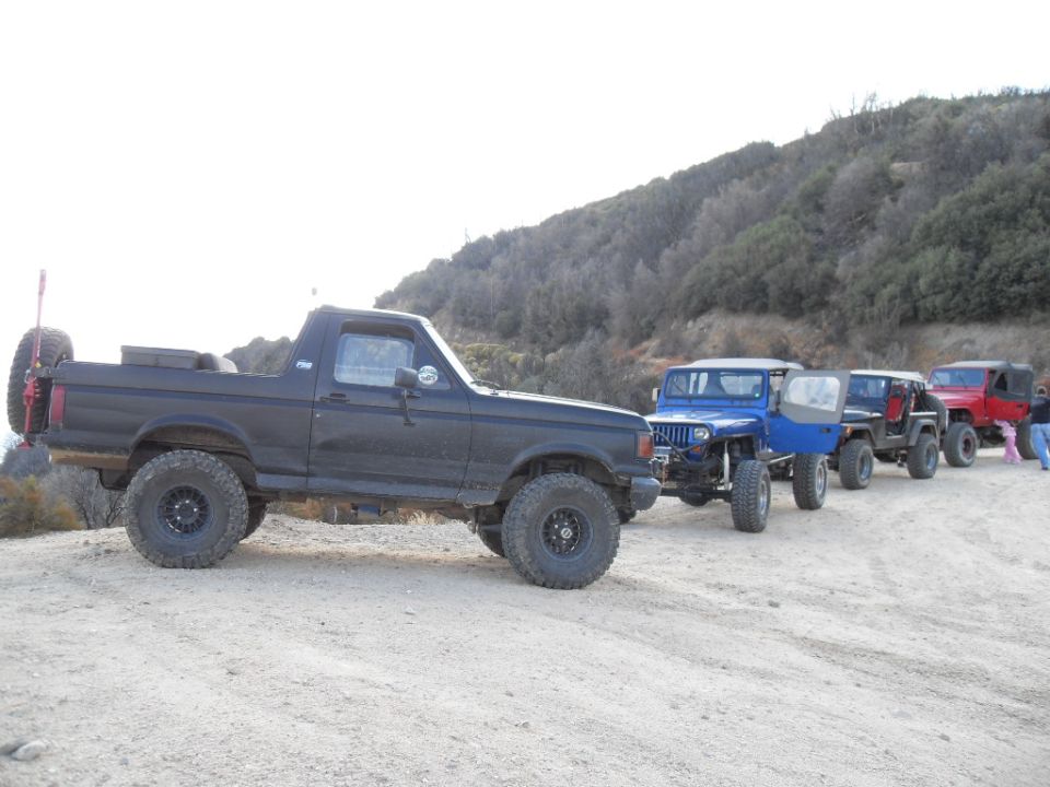 1990 Ford Bronco parked on a dirt road with several Jeeps behind it