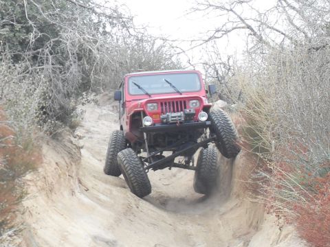 1990 Ford Bronco - A red Jeep Wrangler navigates a challenging off-road trail, with one side of the vehicle significantly higher than the other.
