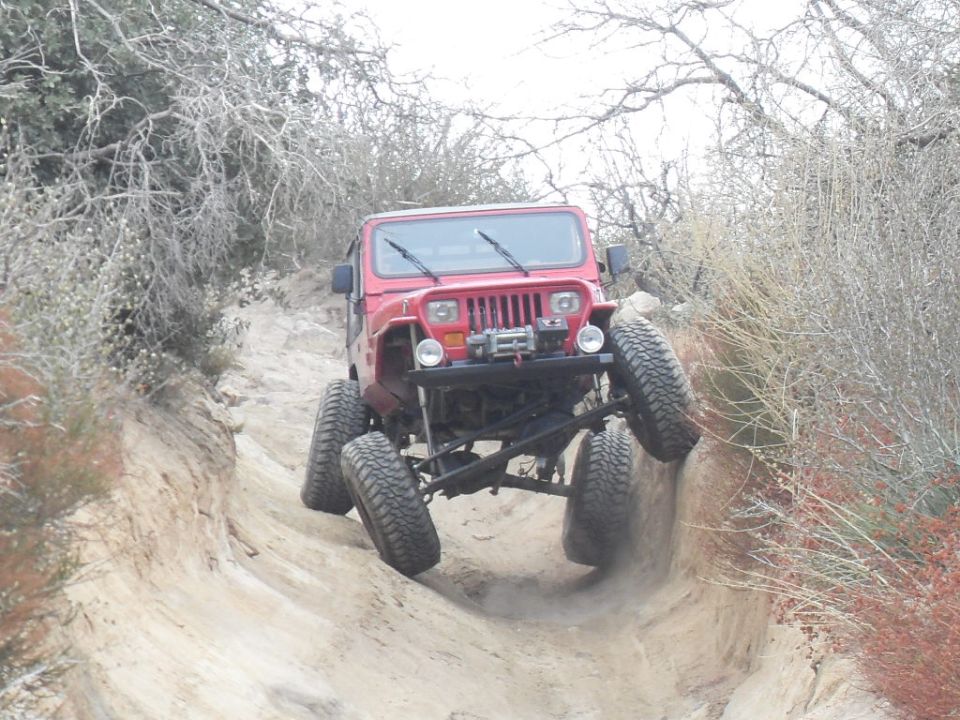 Red Jeep Wrangler climbing a steep, sandy trail with its front wheels high off the ground