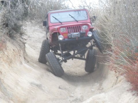 1990 Ford Bronco - A red Jeep Wrangler navigates a challenging off-road trail with its wheels at steep angles.