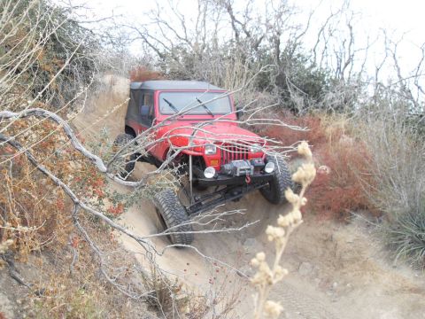 1990 Ford Bronco - This red Jeep Wrangler navigates a steep, dusty trail, its off-road capabilities.