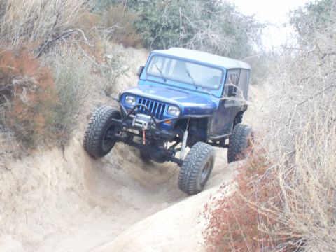 1990 Ford Bronco - A blue Jeep Wrangler navigates a steep, sandy incline on an off-road trail.