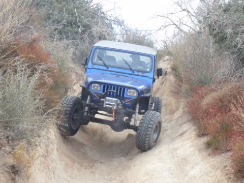 1990 Ford Bronco - This blue Jeep Wrangler is shown off-roading on a dusty, dry trail with sparse vegetation.
