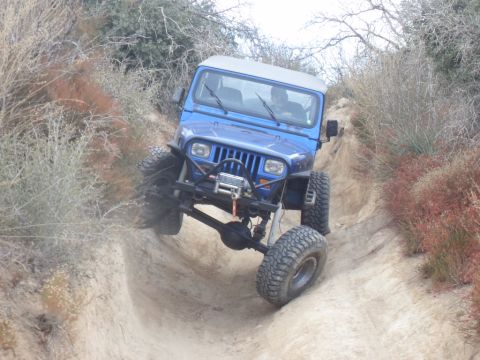 1990 Ford Bronco - Jeep Wrangler tackling an off-road trail with steep inclines and loose dirt.
