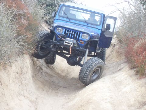 1990 Ford Bronco - A blue Jeep Wrangler navigates a challenging off-road trail, demonstrating its suspension articulation.