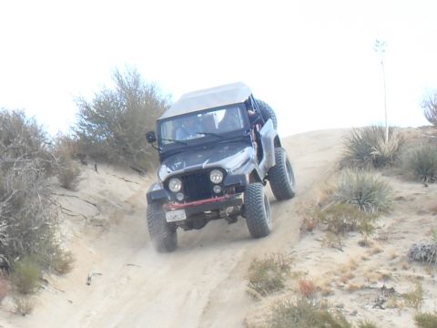 1990 Ford Bronco - A black Jeep CJ-7 navigates a dusty, off-road trail with sparse desert vegetation.