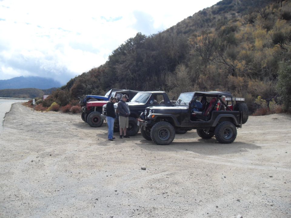 Four off-road vehicles parked on a dirt lot with a hillside in the background