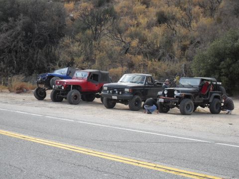 1990 Ford Bronco - Several off-road vehicles are parked on the side of a road with people attending to them.