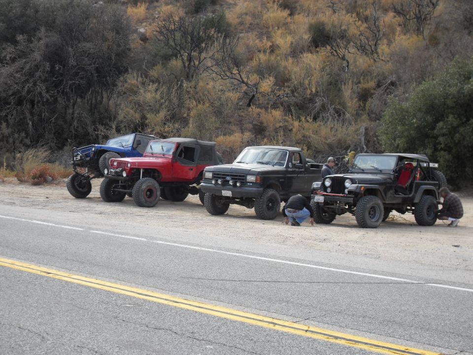 Four modified off-road vehicles parked on a dirt shoulder next to a road