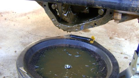 1986 Ford Bronco - Differential housing with gears and draining oil into a black pan.