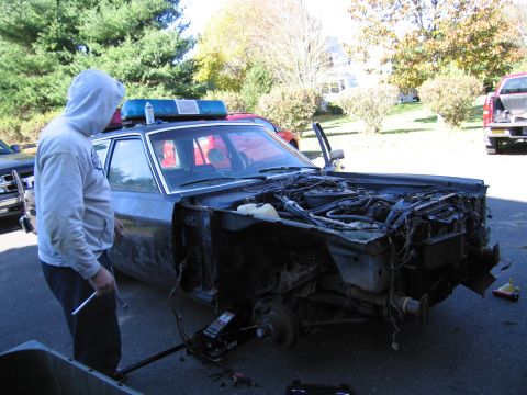 2001 Ford Crown Victoria - Police car undergoing repairs with engine compartment open and front wheels removed.