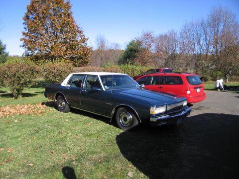2001 Ford Crown Victoria - A dark blue sedan with a white roof and flat tires sits on a grassy lawn next to a red SUV.