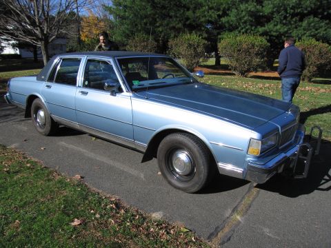 2001 Ford Crown Victoria - This light blue sedan features a push bumper and a black vinyl roof, with two men standing nearby.