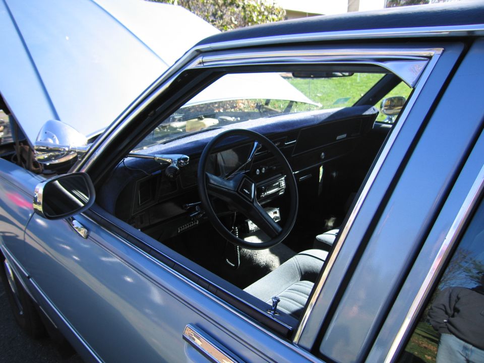 Blue car interior with dark upholstery, steering wheel, dashboard, and open hood
