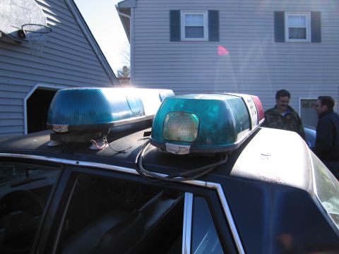 2001 Ford Crown Victoria - A black police car with a light bar on its roof is parked in front of a house.