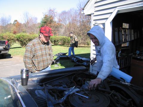 2001 Ford Crown Victoria - Three men work on the engine bay of a car outdoors.
