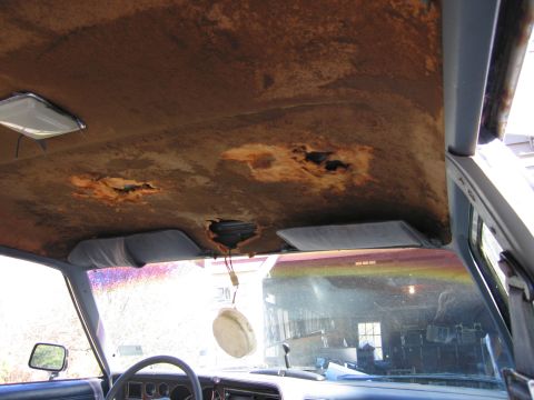 2001 Ford Crown Victoria - The interior of a car shows significant damage to the headliner with visible holes and discoloration.