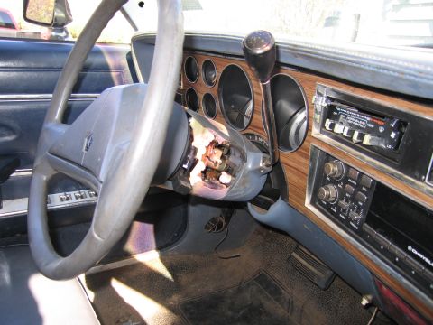 2001 Ford Crown Victoria - The interior of a car shows a damaged steering column and dashboard with wood-grain accents and an aftermarket radio.