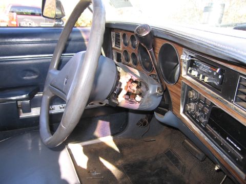 2001 Ford Crown Victoria - The interior of a car shows a damaged steering column and a Chrysler radio unit.