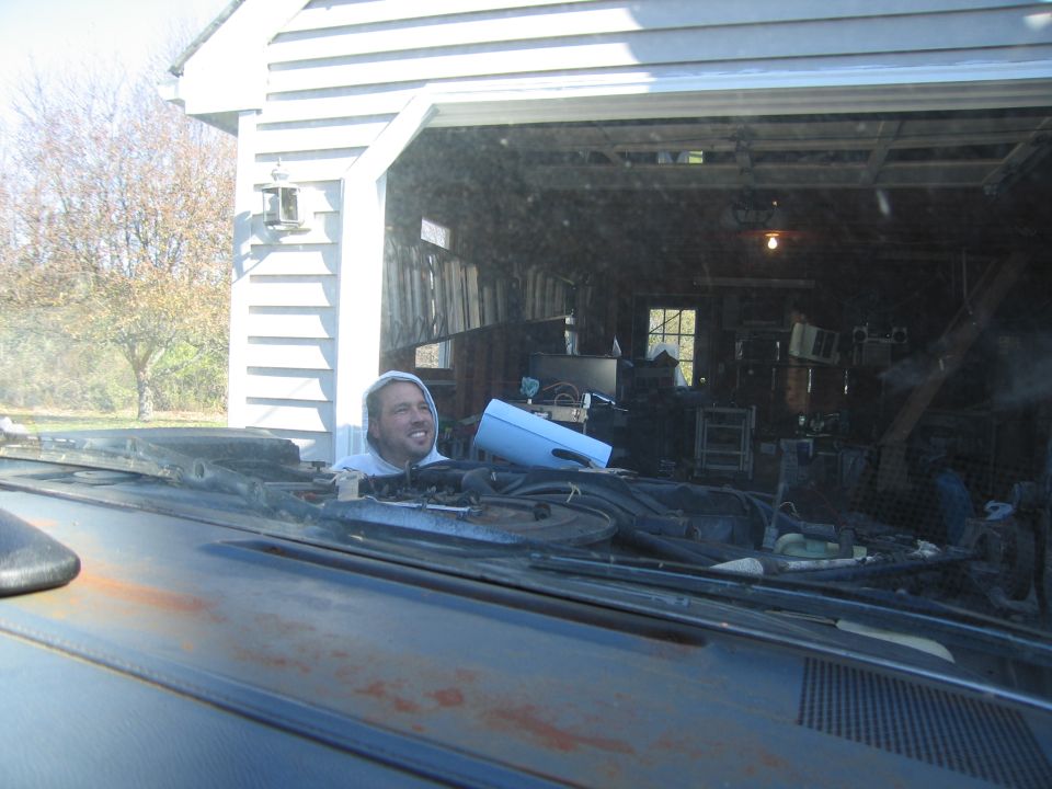 Guy in a hoodie peeking over the dashboard of a car, looking into a cluttered garage