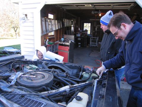 2001 Ford Crown Victoria - Three men examine the engine compartment of a car in a cluttered garage.