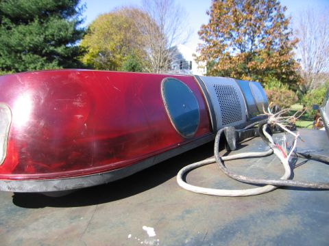 2001 Ford Crown Victoria - Emergency light bar with red lenses and exposed wiring sits on a dark surface outdoors.
