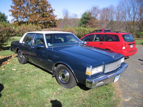 2001 Ford Crown Victoria - A dark blue sedan with a white roof is parked on grass, with a red SUV behind it.