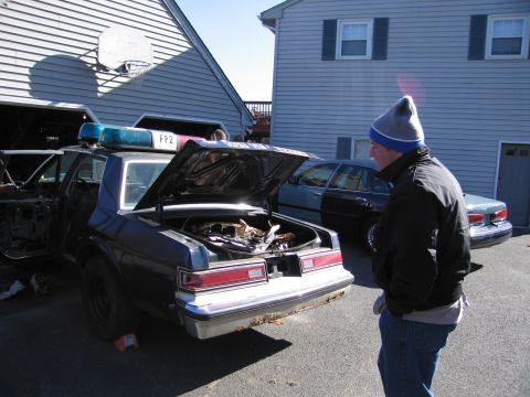2001 Ford Crown Victoria - A man stands near a disassembled police car with its trunk and driver's door open.