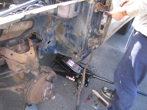 2001 Ford Crown Victoria - Mechanic works on the door hinge area of a car, with a jack supporting the frame.