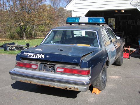 2001 Ford Crown Victoria - A dark blue police car with a light bar sits in a driveway, showing significant wear and tear.