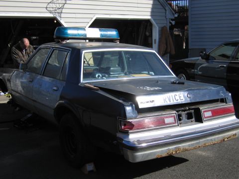 2001 Ford Crown Victoria - A police car with a light bar is parked in front of a garage, with another vehicle visible behind it.