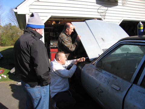 2001 Ford Crown Victoria - Three men are gathered around a car with its hood open, appearing to work on the engine bay.