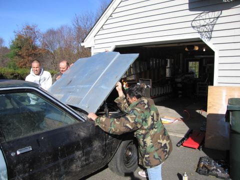 2001 Ford Crown Victoria - Three men are working on the engine of a car with its hood open in front of a suburban garage.