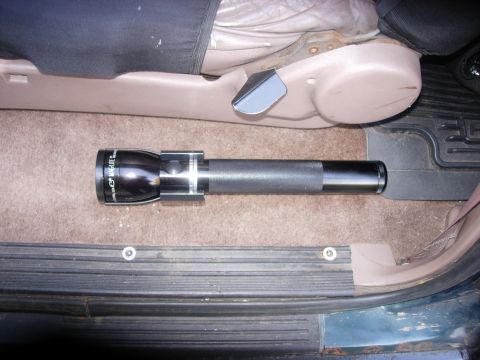 1993 Ford Bronco - A Maglite flashlight rests on the floor mat of a vehicle, near the driver's seat.