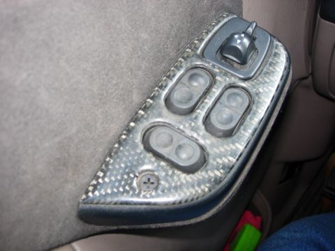 1993 Ford Bronco - Close-up of a car's interior door panel showing power window controls with aftermarket carbon fiber trim.