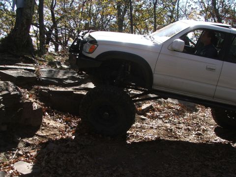 1996 Ford Bronco - This white SUV is shown off-roading on a rocky trail with dense trees in the background.