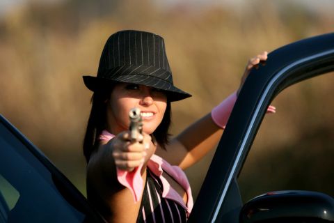 2003 Mercury Marauder - A woman in a fedora and pink attire aims a handgun while leaning out of a car door.