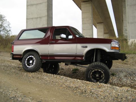 1996 Ford Bronco - This lifted Ford Bronco is shown from a 3/4 front angle under a concrete overpass.