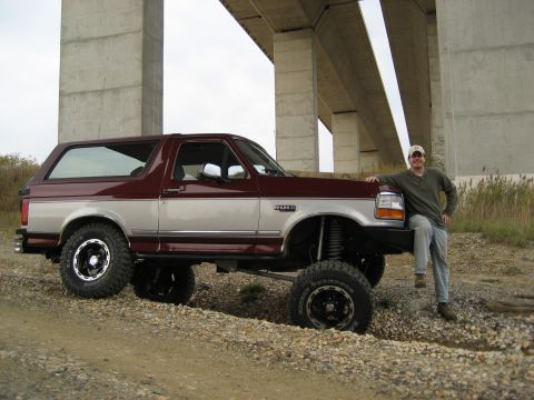 1996 Ford Bronco - A man poses with a lifted two-tone maroon and silver 1996 Ford Bronco parked under a bridge.