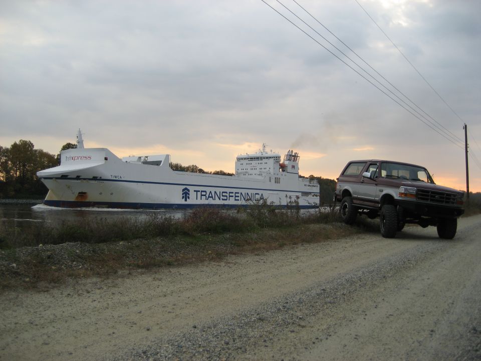 1996 Ford Bronco parked on a dirt road next to a large cargo ship