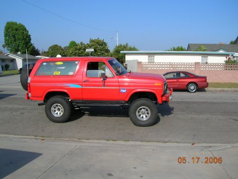 1985 Ford Bronco - This red 1985 Ford Bronco features a lifted suspension and off-road tires, seen parked on a residential street.