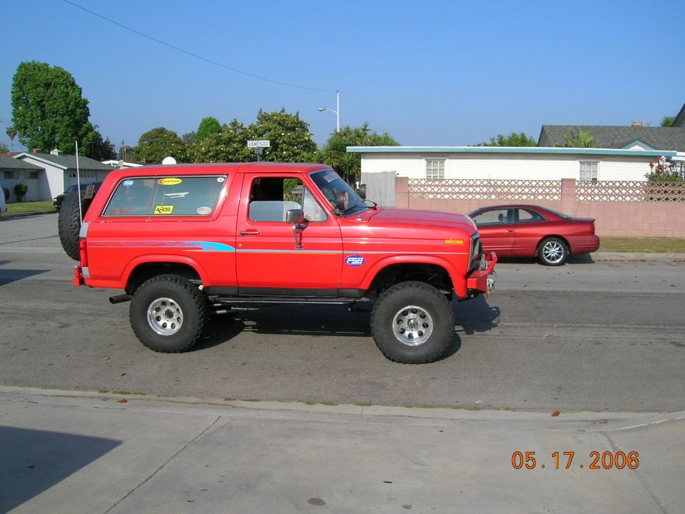 Lifted red Ford Bronco in side profile with rear tire carrier and winch bumper on a street