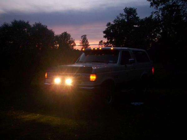 White 1991 Ford Bronco parked at dusk with headlights on.