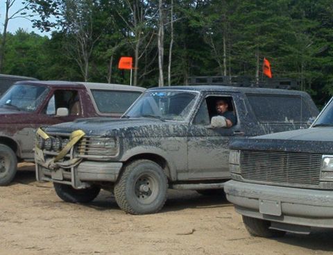 1993 Ford Bronco - Three muddy Broncos are parked off-road, with one driver visible behind the wheel.