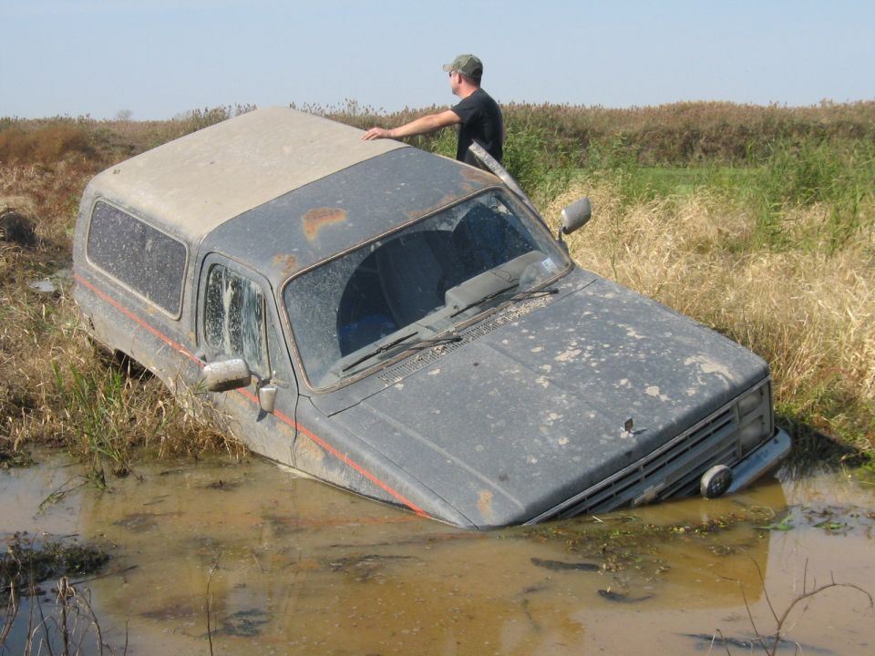 Gray SUV stuck in mud, front quarter view. Appears to be a 1990 Ford Bronco