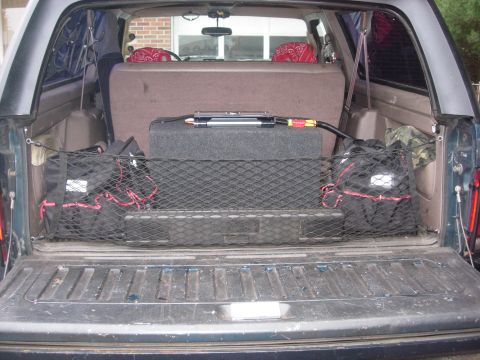 1993 Ford Bronco - The cargo area of a vehicle is shown with a subwoofer, storage bags, and a cargo net.