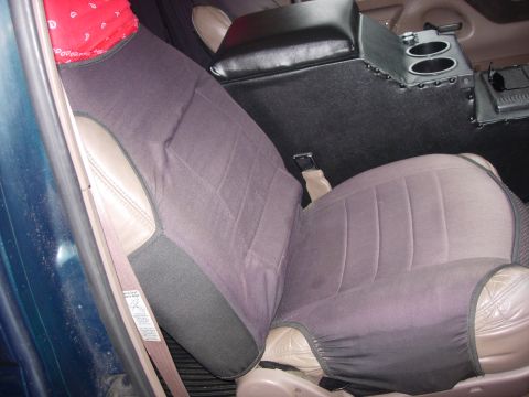 1993 Ford Bronco - The interior of a vehicle shows cloth seat covers over leather seats, a center console with cup holders, and a red bandana on the headrest.