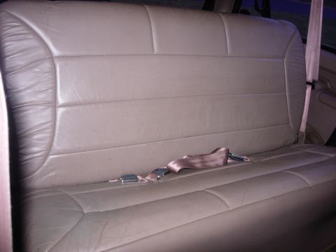 1993 Ford Bronco - The interior of a vehicle shows a tan leather rear bench seat with a seatbelt partially buckled across it.