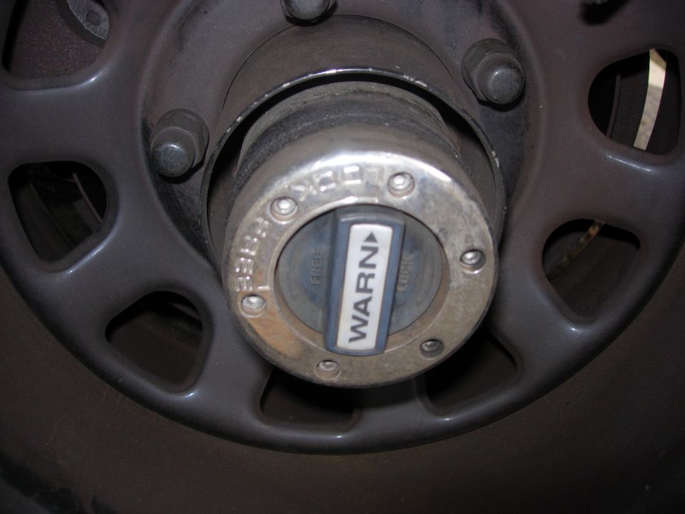 Close-up of a Warn manual locking hub on a vehicle wheel. The hub is set to 'WARN'